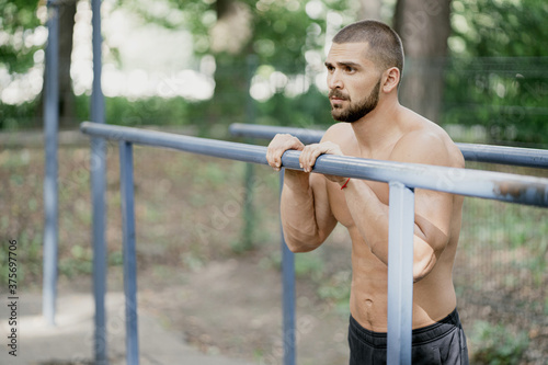 young man male. doing strength training on the machines. sports stadium. athletic body. short hair and beard. outdoor training on uneven bars