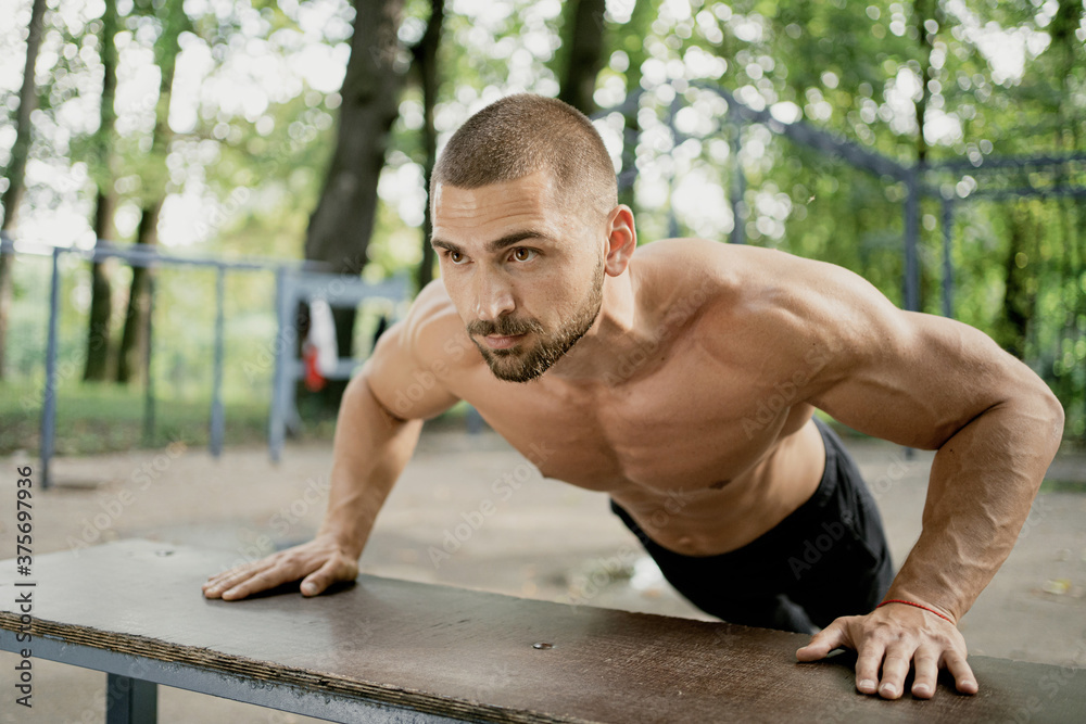Obraz premium doing the plank exercise on the simulator thinks about your body and health. a satisfied man of athletic build. stadium in the Park. short hair, beard, naked torso. Caucasian appearance