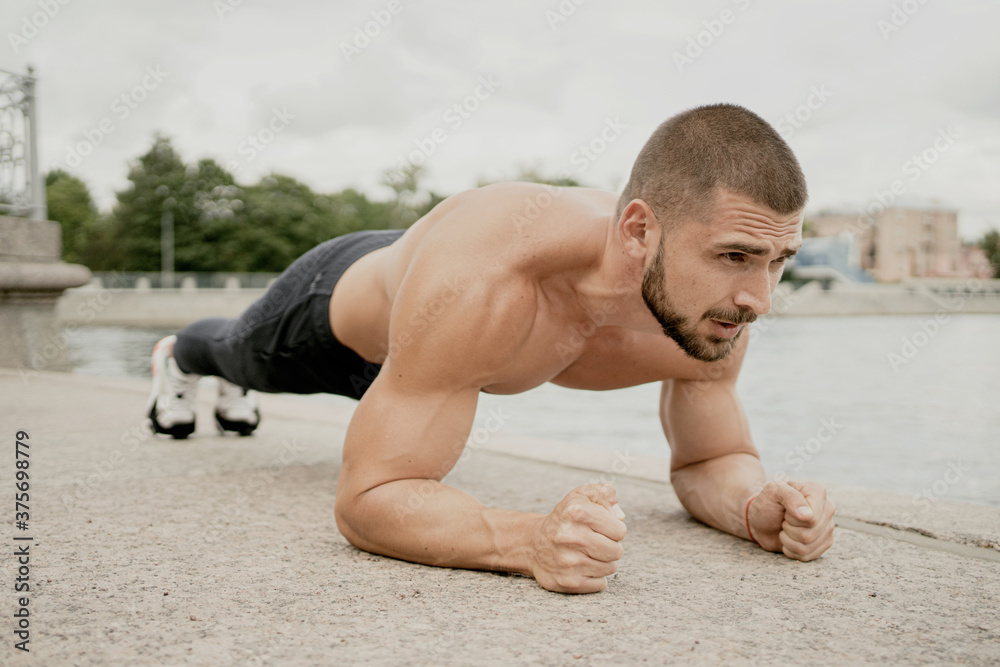 Obraz premium portrait of a sporty dark-haired man doing a plank exercise on the street, tense looking ahead. short haircut brunette barbershop. Caucasian appearance