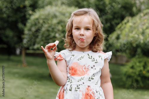 Funny kid girl eating sandwich outdoors. Having fun. Looking at camera. Posing over nature background. Healthy food. Childhood. © Andriy Medvediuk