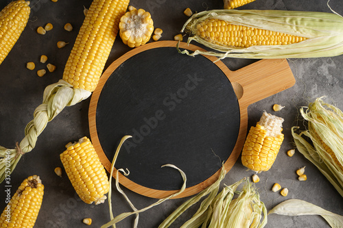 Ripe corn on a cutting board on a gray background, space for text. Flat lay.