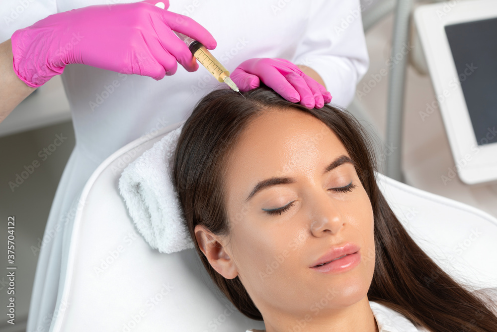 Naklejka premium Cosmetologist does prp therapy against hair loss and anti-dandruff of a beautiful brunette woman in a beauty salon. Aesthetic cosmetology concept, hair treatment.