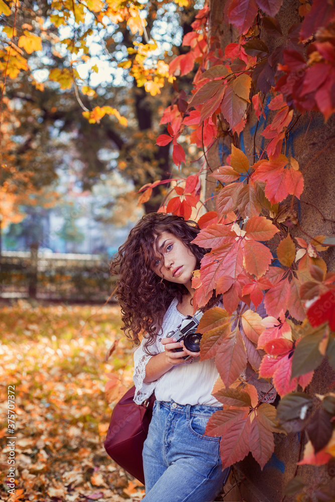 Beautiful young woman with curly hair, blue eyes and freckles holding a vintage camera