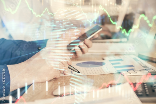 Double exposure of man's hands holding and using a digital device and forex graph drawing. Financial market concept.