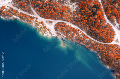 Aerial view of a blue lake near the shore with a beautiful autumn forest with orange trees and gravel roads. photo