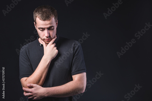 Portrait of an emotional handsome young man, on a black background in the studio, who stands in a brooding pose. Expression of emotions and feelings