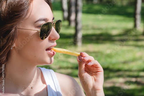 Beautiful, young woman eating fries in the street. The concept of fast food, food delivery and lunch in nature