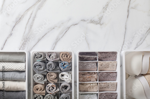 Womans underwear, pajamas and socks neatly folded and placed in closet organizer drawer divider on white marble table.