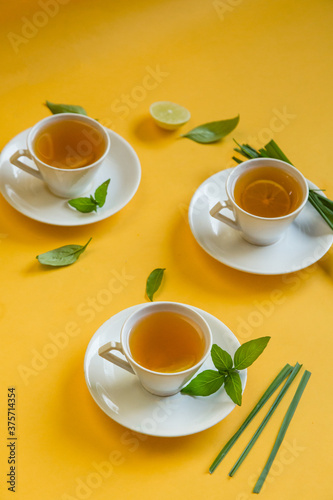 Herbal green tea with lemongrass in glass cup with fresh limes. Top view of three white cups of Lemon Grass Drink on a Yellow Background.