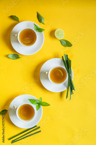 Herbal green tea with lemongrass in glass cup with fresh limes. Top view of three white cups of Lemon Grass Drink on a Yellow Background.