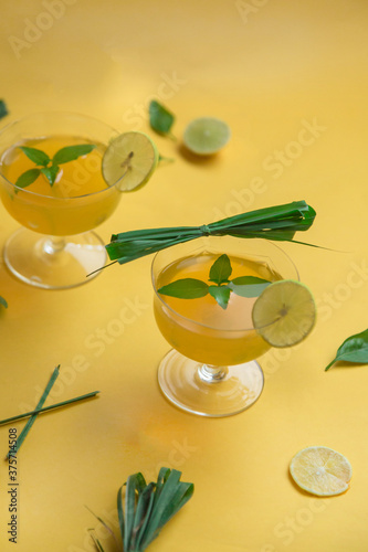 Herbal green tea with lemongrass in glass cup with fresh limes. Top view of two cups of Lemon Grass Drink on a Yellow Background.