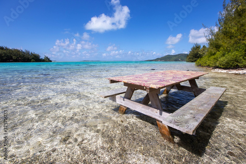 Picnic table in shallow, clear, tropical island ocean water on a private motu