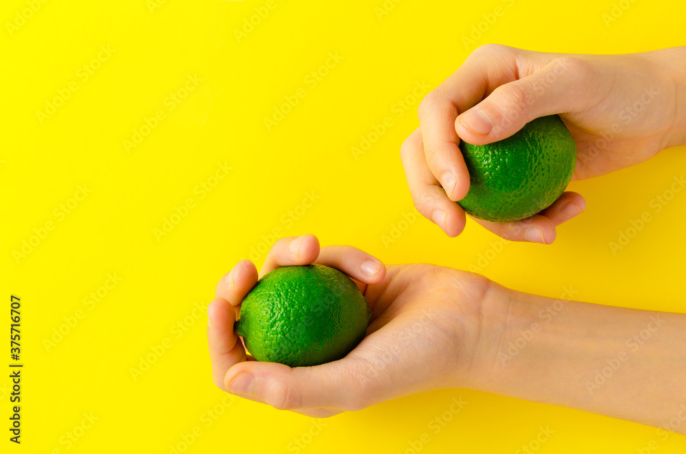 A children's hand holding limes in her hands on yellow background. This fresh fruit contains vitamin c and can be used as an ingredients for many dishes. Healthy background concept. A children's hand holding limes in her hands on yellow background. This fresh fruit contains vitamin c and can be used as an ingredients for many dishes. Healthy background concept.