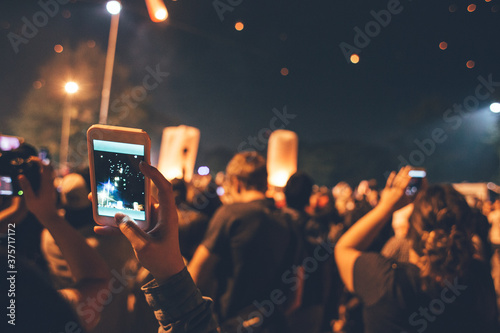 Festival time - People taking photos on phone of fire lanterns flying in the night sky photo