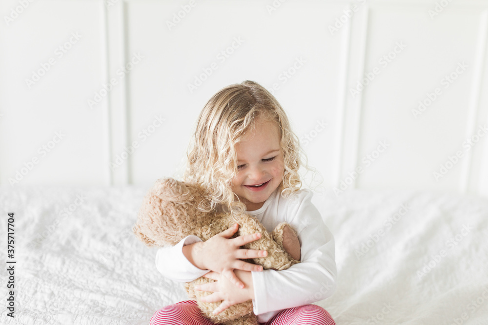 Happy young girl wearing red and white striped pajamas hugs teddy bear