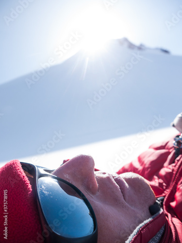 Headshot of exhausted alpinist lying under the snowy mountain