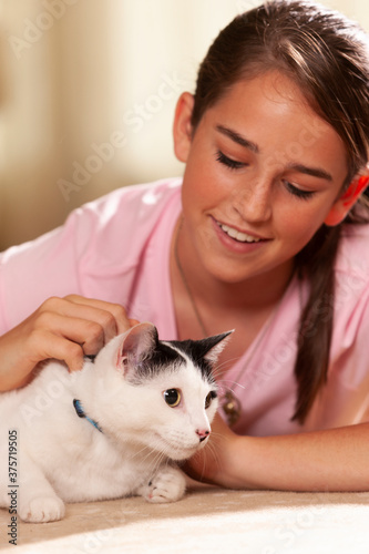 Portrait of teenage Caucasian girl lying on rug in living room petting her pet cat, cat looking off camera 