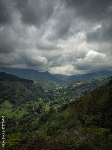 Moody vertical landscape of mountains and green valley and forest with trees with a beautiful dark sky with clouds in Salento, Colombia
