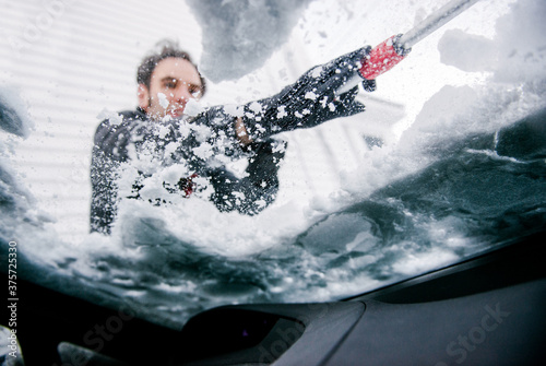 Man removes snow from the windshield of his car photo