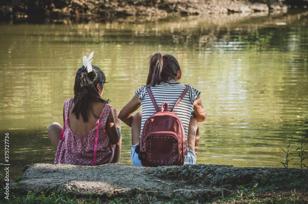 Unrecognizable two little girls sitting by a lake. Concept of childhood.
