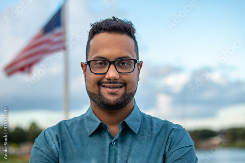 Happy smiling hispanic business man small business owner, company leader or sales manager, male hispanic ceo, successful college looking at camera standing in front of US Flag, headshot portrait
