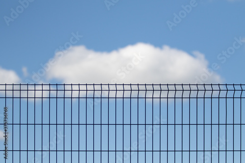 Metal grid against the blue sky with white clouds. © Prikhodko