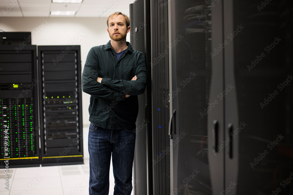 Young IT engineer standing near datacenter servers Young IT engineer standing near datacenter servers
