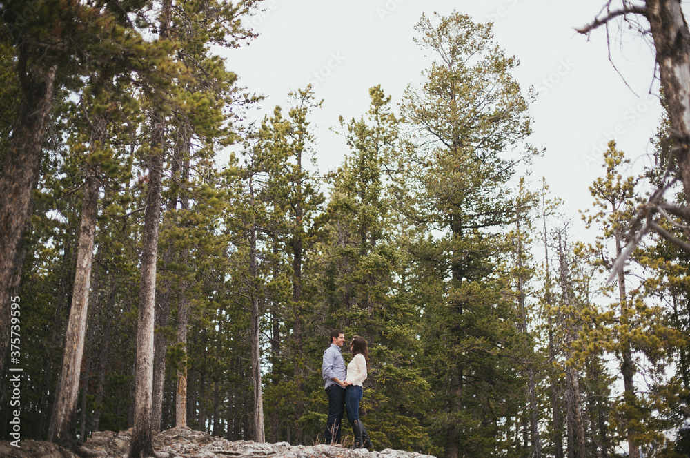 Engaged couple standing and hugging, laughing in forest in Banff National Park Engaged couple standing and hugging, laughing in forest in Banff National Park