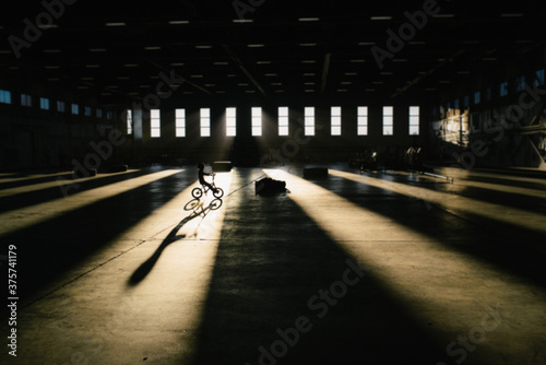 Child coasts on his bike, through a beam of light, casting a long shadow photo