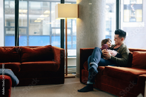 Hip young dad spending time with daughter inside - laughing on couch photo