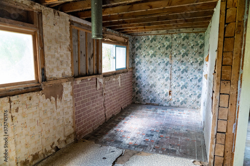 Interior of an abandoned room inside a home in Bannack Ghost town. Peeling wallpaper and cracking floorboards, with exposed beams in ceiling © MelissaMN