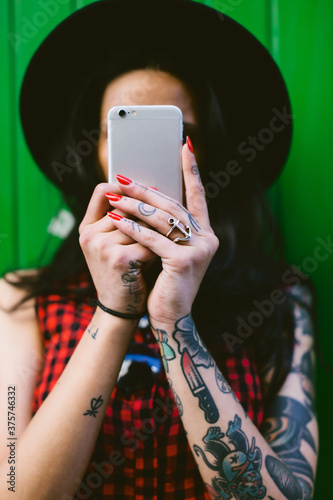 Young alternative woman covering her face with her smartphone.