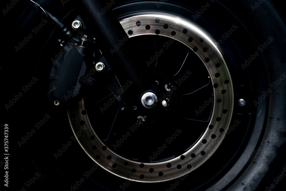 Abstract dark tone beside veiw of Disc Brake of motorcycle with a sparkling light.