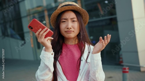 Bad day and bad news. Portrait of displeased asian woman receiving frustrating message on smartphone feeling shocked shrugging shoulders having doubts. Airport.