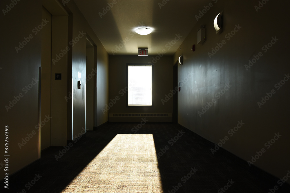 An image of sunlight streaming through a window in a very dark hallway of a run down apartment building. An image of sunlight streaming through a window in a very dark hallway of a run down apartment building.