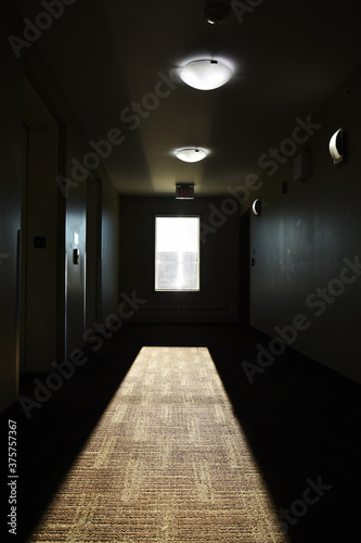 An image of sunlight streaming through a window in a very dark hallway of a run down apartment building. 