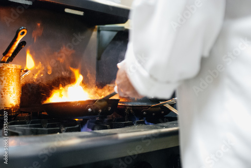 A chef cooks with a flaming fry pan in a restaurant kitchen