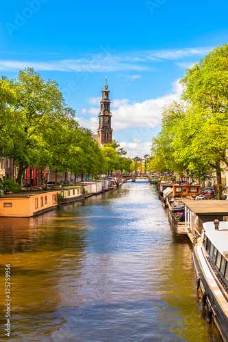 Tranquil Amsterdam canal with Dutch houseboats Westerkerk Church Cathedral on sunny blue sky summer day