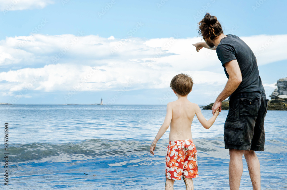 Boy and his dad stand together by the ocean Boy and his dad stand together by the ocean