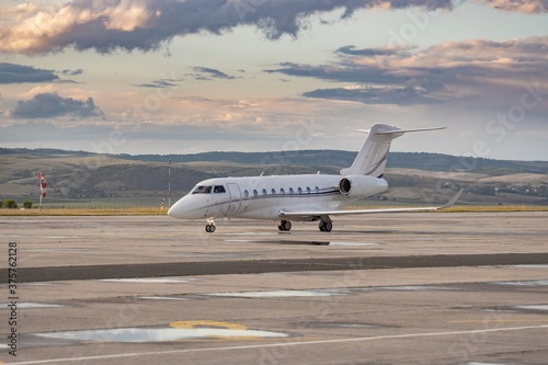 White small private twin-engine business jet on airport apron. Attractive landscape dramatic grey orange clouds, puddles after rain weather. Modern technology in fast transportation, business travel. photo