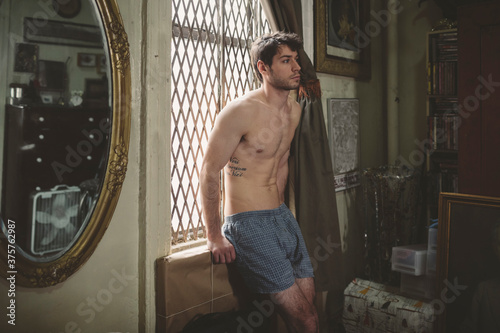 Man in Boxer Shorts Sitting by Window of Bedroom