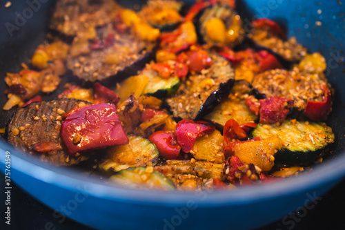 plant-based food, vegan eggplant zucchini and red pepper mix getting sauteed on a pan with mixed spices and fresh tomatoes