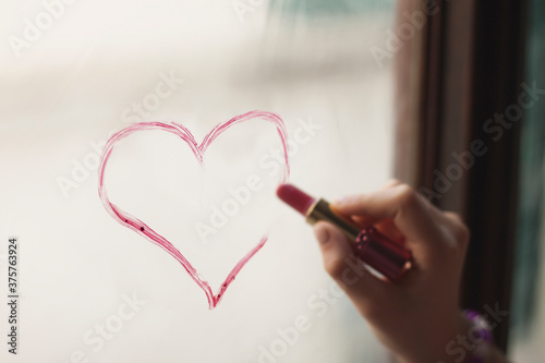 Woman drawing with lipstick a heart on the window