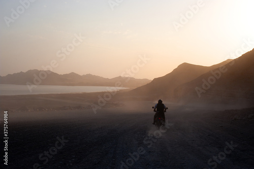 Motorcyclist rides his bike on a dirt and wild road at sunset towards the Caspian Sea