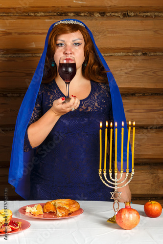 On the eve of Rosh Ashan, a Jewish woman stands next to burning candles with a glass of Kiddush wine in her hand. photo