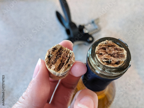 Broken Wine Cork in Half in Lady's Hand and Stuck in the Wine Bottle with a Black Bottle Opener on the Counter in the Background - Typical 2020