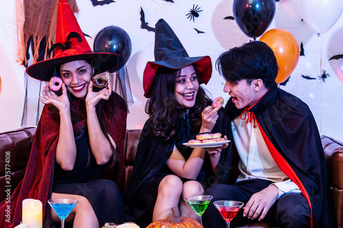 Asian Happy friends sitting on sofa in costumes and makeup on a celebration of Halloween enjoy food and having fun in party, Celebration of Halloween..
