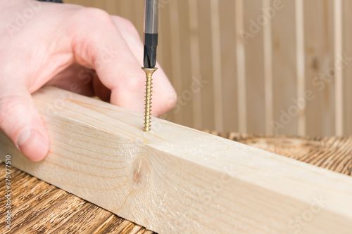 hands hold a wooden block and screw into it a screw with a screwdriver, closeup