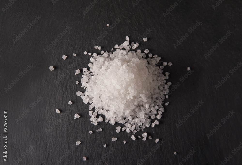 Pila de sal de mar grano grande sobre mesa de piedra negra.