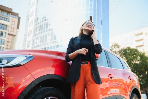 Woman using mobile phone, communication or online application, standing near car on city street or parking, outdoors. Car sharing, rental service or taxi app.